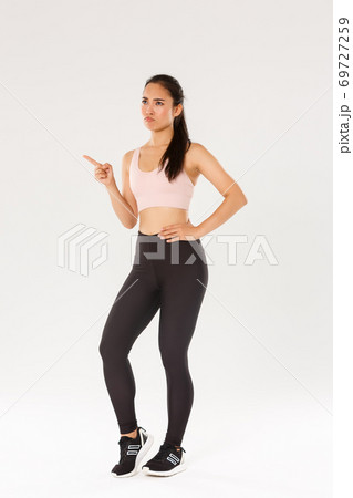 Sport, gym and healthy body concept. Full length of skeptical and displeased female athlete, asian sportswoman sulking and frowning disappointed, pointing finger upper left corner and complaining 69727259