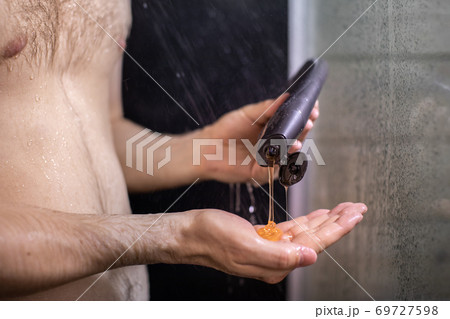 young naked man pours body wash gel on palm while showering on black backdrop young naked man pours body wash gel on palm while showering on black backdrop 69727598