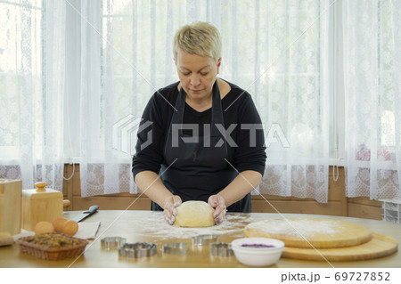 Caucasian beautyful woman housewife kneading dough on wooden antique table. Caucasian beautyful woman housewife kneading dough on wooden antique table. 69727852