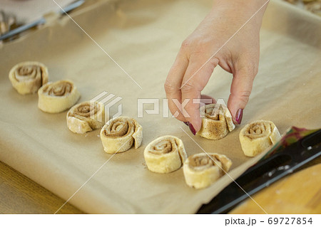 A portrait of the hands of a housewife who lays cinnamon rolls on baking paper. A portrait of the hands of a housewife who lays cinnamon rolls on baking paper. 69727854