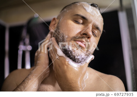 Close up handsome man with closed eyes washes face, beard while taking shower 69727935