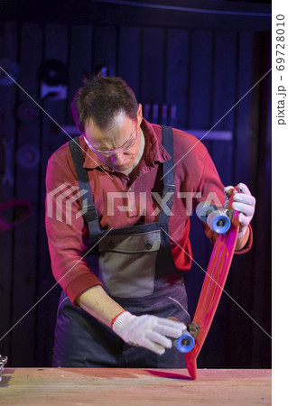 middle-aged man in jumpsuit testing plastic kids skateboard in carpentry 69728010