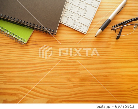 木製作業机の上に並べた仕事アイテムと文房具（横型-下余白） 69735912