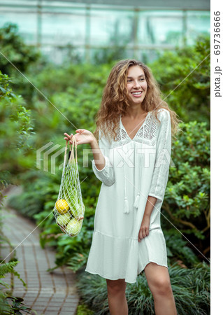 Woman in white dress standing with bags of different vegetables 69736666