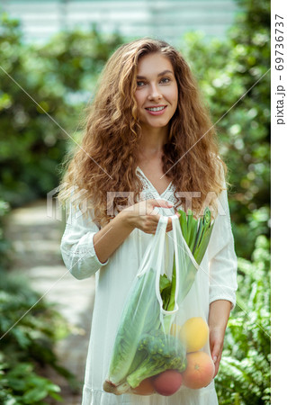 Woman in white dress holding a bag with veggies 69736737