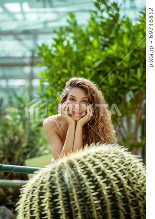 Pretty young woman standing near the cactus and looking thoughtful Pretty young woman standing near the cactus and looking thoughtful 69736812