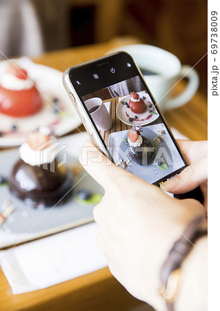 ケーキの写真をスマホで撮影をする若い女性手元 69738009
