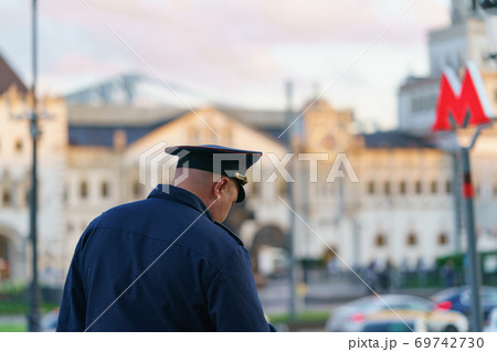Policeman at the Moscow city street. He wear blue uniform. Old architecture. Red letter M - the sign on entrance into subway. Back / rear view. 69742730