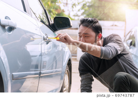 Thief male stealing secretly used screwdriver to open the car door in parking. Car robbery concept. Thief male stealing secretly used screwdriver to open the car door in parking. Car robbery concept. 69743787