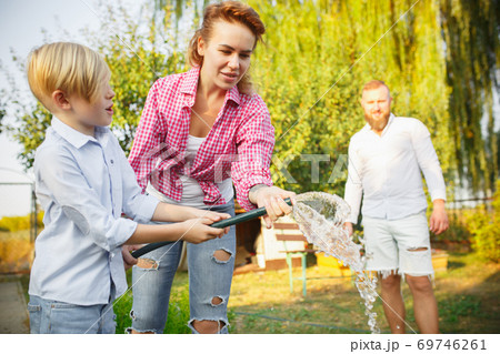 Happy family during watering plants in a garden outdoors. Love, family, lifestyle, harvest concept. 69746261