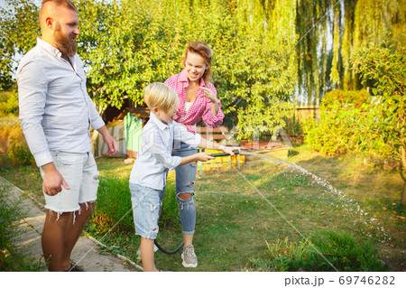 Happy family during watering plants in a garden outdoors. Love, family, lifestyle, harvest concept. Happy family during watering plants in a garden outdoors. Love, family, lifestyle, harvest concept. 69746282