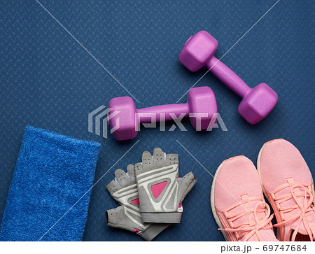 a pair of purple dumbbells, sports gloves and pink gym shoes on a blue neoprene mat a pair of purple dumbbells, sports gloves and pink gym shoes on a blue neoprene mat 69747684