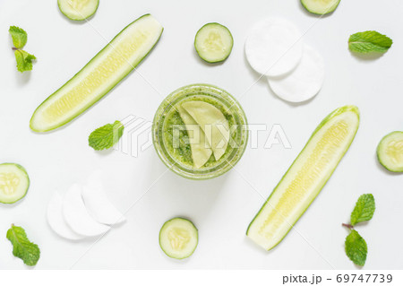 Cucumber eyes mask or makeup remover pads made with natural ingredients for healthy skin care. Top view of cucumber slice, mint leaf, facial cotton pad and jar on white table. Homemade beauty product. Cucumber eyes mask or makeup remover pads made with natural ingredients for healthy skin care. Top view of cucumber slice, mint leaf, facial cotton pad and jar on white table. Homemade beauty product. 69747739