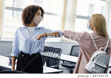 Social distancing and modern greeting during quarantine. African american and european women in protective masks came to work and greet each other with their elbows 69749270