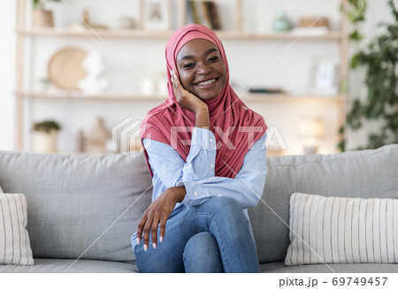 Portrait of happy black muslim woman in hijab on couch at home Portrait of happy black muslim woman in hijab on couch at home 69749457