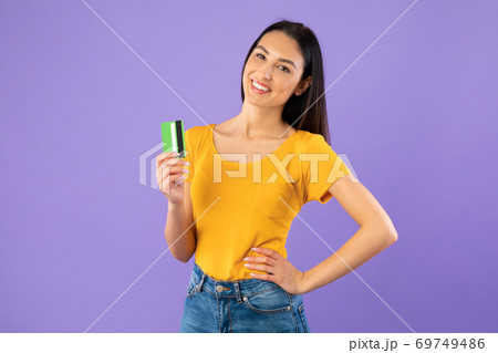 Woman holding credit card at pastel purple studio wall Woman holding credit card at pastel purple studio wall 69749486