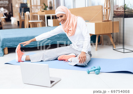 Arab girl stretching and looking at laptop at home Arab girl stretching and looking at laptop at home 69754008
