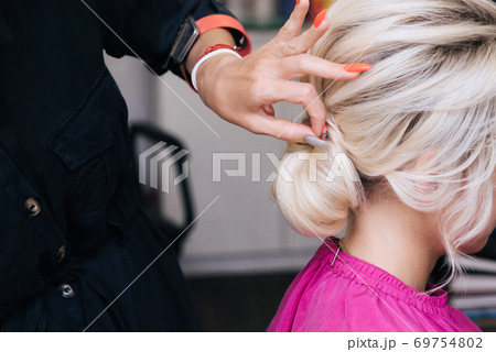 hair stylist makes her hair into a bun on the head of a blonde girl with long hair 69754802