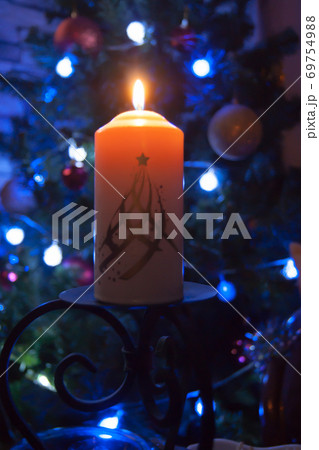 A large candle burns against the background of a garland with shining lights. Vertical photo 69754988