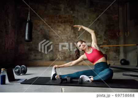 Girl stretching or yoga in gym using a laptop with online training.  69758668