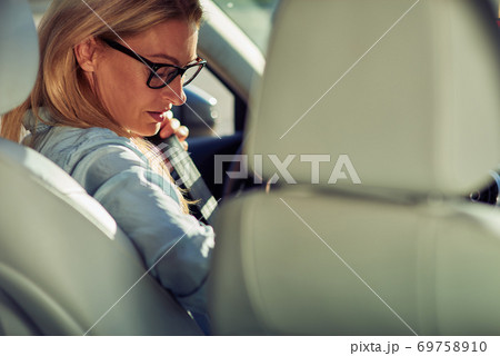 Rear view of a middle aged caucasian woman, business lady sitting behind steering wheel of her car and fastening seat belt Rear view of a middle aged caucasian woman, business lady sitting behind steering wheel of her car and fastening seat belt 69758910