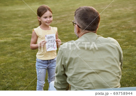 I love you daddy. Father and his cute little daughter celebrating Happy Fathers Day in park on a warm day, small girl giving her father handmade postcard and smiling 69758944