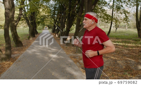 Side view of elderly sport runner man training. Workout cardio outside in city park at morning Side view of elderly sport runner man training. Workout cardio outside in city park at morning 69759082