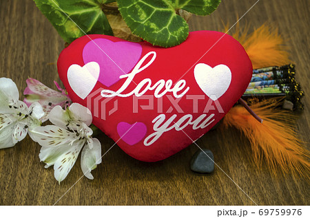 Flowers, colored feathers, leaves next to a red heart with the words "I love you" on polished boards 69759976