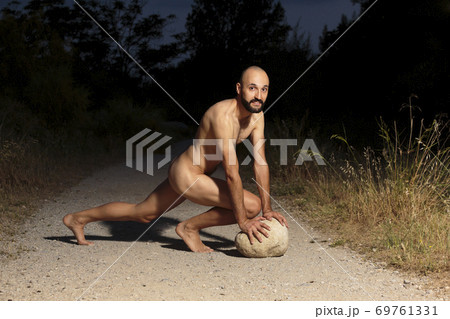 Young male athlete fully naked crouching on a trail at night looking at camera Young male athlete fully naked crouching on a trail at night looking at camera 69761331