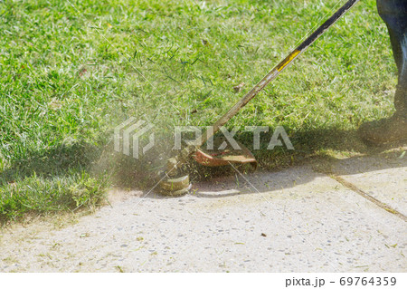 A municipal worker in an lawn mower mows fresh, green grass on the lawn near residential building. A municipal worker in an lawn mower mows fresh, green grass on the lawn near residential building. 69764359