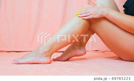 The young woman with perfect body applying refreshing cream body lotion on her legs. Concept of 69765223