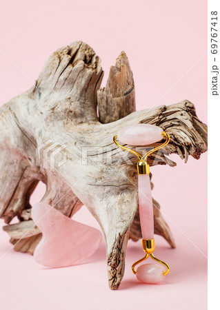 Modern luxury stylish beauty concept - Facial massage kit and wooden root on pink background. Face roller and gua sha massager made from natural pink stones, wellbeing, face fitness 69767418