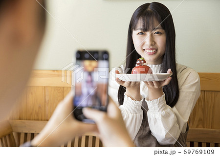 カフェで可愛いケーキと写真を撮る若い女性 女子大生の写真素材