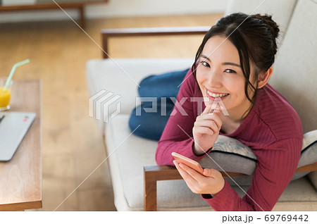 テレワーク中にソファーに寝転がってスマホを操作する女性 テレワーク中にソファーに寝転がってスマホを操作する女性 69769442