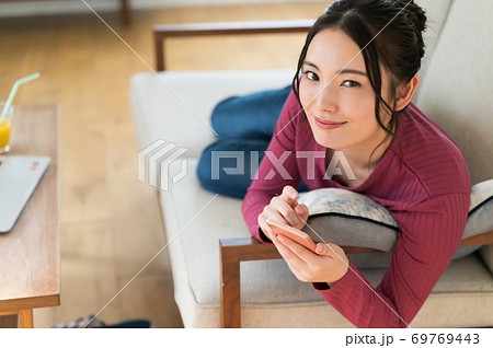 テレワーク中にソファーに寝転がってスマホを操作する女性 69769443
