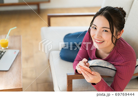 テレワーク中にソファーに寝転がってスマホを操作する女性 テレワーク中にソファーに寝転がってスマホを操作する女性 69769444
