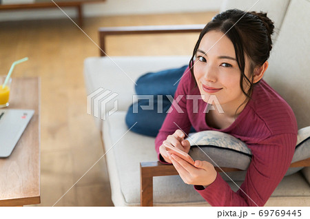 テレワーク中にソファーに寝転がってスマホを操作する女性 69769445