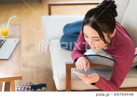 テレワーク中にソファーに寝転がってスマホを操作する女性 69769446