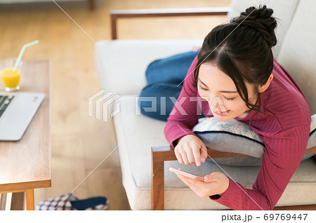 テレワーク中にソファーに寝転がってスマホを操作する女性 69769447