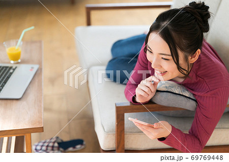 テレワーク中にソファーに寝転がってスマホを操作する女性 テレワーク中にソファーに寝転がってスマホを操作する女性 69769448