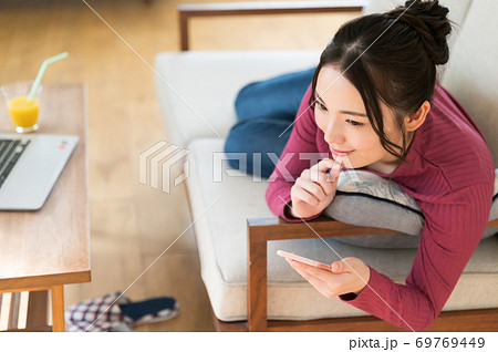 テレワーク中にソファーに寝転がってスマホを操作する女性 69769449