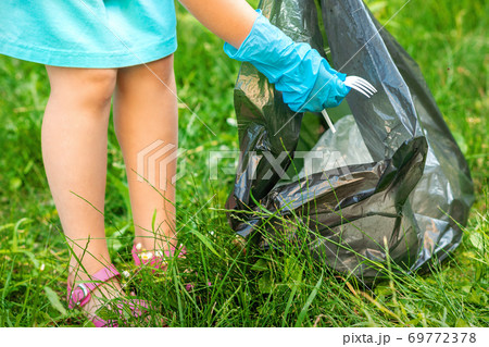 Child picks plastic trash from grass Child picks plastic trash from grass 69772378