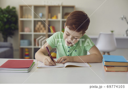 Smiling little schoolboy doing homework sitting at a desk in his bright room. Smiling little schoolboy doing homework sitting at a desk in his bright room. 69774103