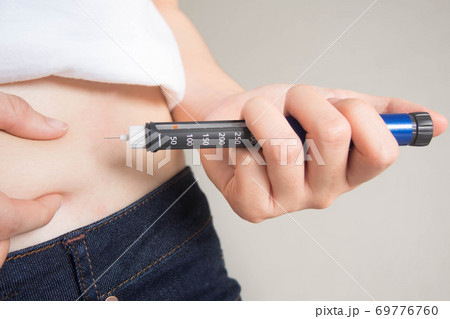 Close up of female diabetes patient making subcutaneous insulin injection into her abdomen with insulin pen syringe at home. Diabetes, health care and medical concept. Diabetes World Day. 69776760