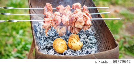 Man prepares barbecue meat with potatoes 69779642