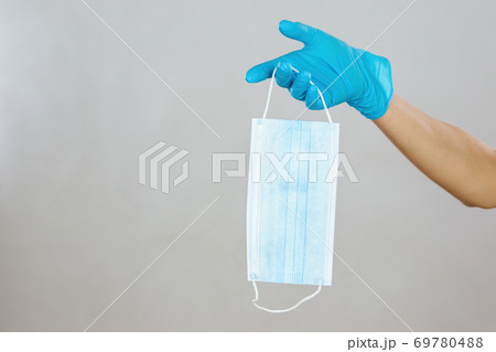 Hand in blue rubber gloves holding a surgical mask in studio with copy space Hand in blue rubber gloves holding a surgical mask in studio with copy space 69780488