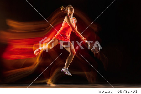Professional female tennis player isolated on black studio background in mixed light Professional female tennis player isolated on black studio background in mixed light 69782791