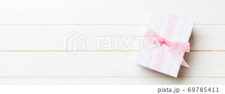 Beautiful gift box with a colored bow on the white wooden table. Top view banner with copy space for you design Beautiful gift box with a colored bow on the white wooden table. Top view banner with copy space for you design 69785411