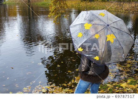 woman under umbrella stands on the shore of an autumn lake.. 69787517