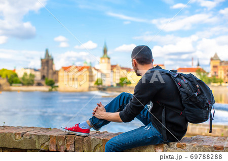 A tourist guy with a backpack sits on the embankment in Prague overlooking the Vltava river 69788288